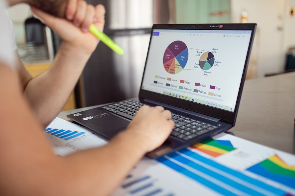 Person analyzing financial charts and graphs on a laptop with colorful documents, showcasing market analysis.